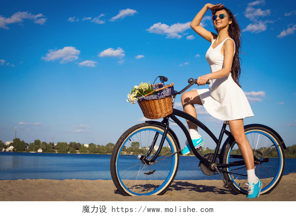 年轻漂亮的女孩在沙滩上骑自行车美丽的年轻女子在沙滩上巡洋舰自行车